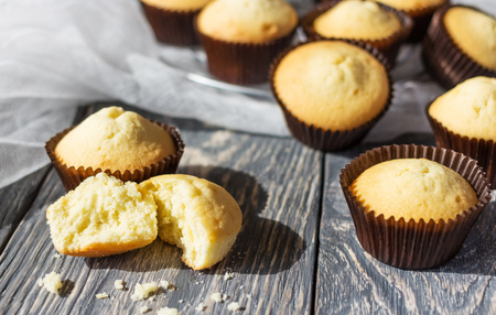 Broken piece of cake, lots of cupcakes in molds on wooden surfaceの写真素材