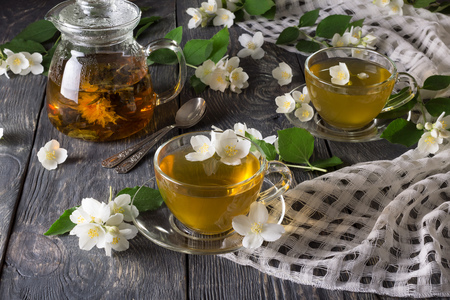 Teapot with herbal tea, cups with drink, scattered Jasmine flowers on gray surfaceの写真素材