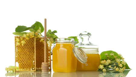 Two jars of honey, frames with honeycombs and spoon, next to Linden flowers, isolated on whiteの写真素材