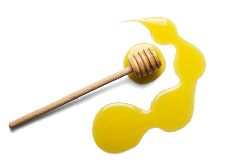 Puddle of liquid sweet honey and wooden stirrer isolated on whiteの写真素材