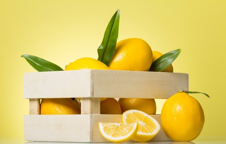 Wooden box full of lemons, near citrus pieces, on bright yellowの写真素材