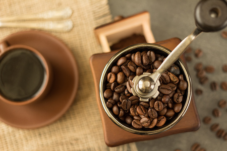 Mill is filled with coffee beans, next to Cup of hot coffeeの写真素材