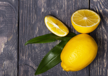 Whole lemon and sliced pieces lie on wooden surfaceの写真素材