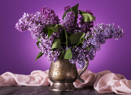 Bouquet of lilac in an old vase decorated with pink fabric, on purpleの写真素材