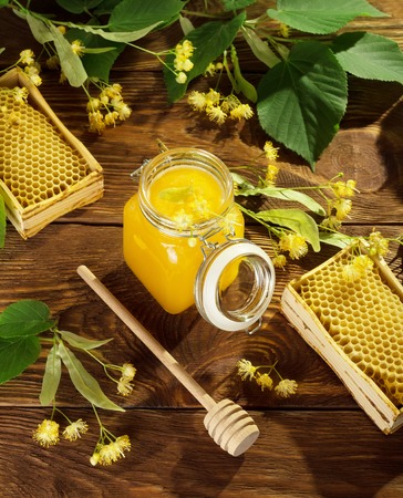 Jar of lime honey, frames with bee cells, spindle and Linden flowers on tableの写真素材