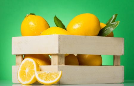 Box of lemons, near the cut fruit, on greenの写真素材