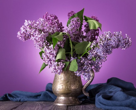 Bouquet of fragrant lilacs in vintage vase on background of fabricの写真素材