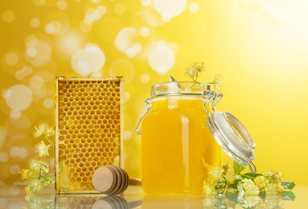 An open jar of honey, honeycombs and wooden spoon on yellow backgroundの写真素材