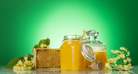 Two glass jars of honey, wooden frame with honeycomb and Linden branches, on green backgroundの写真素材