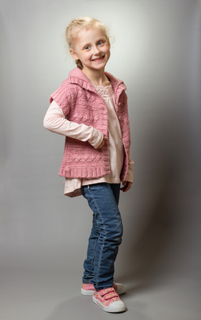 Small smiling girl stands in handmade jacket, on grayの写真素材