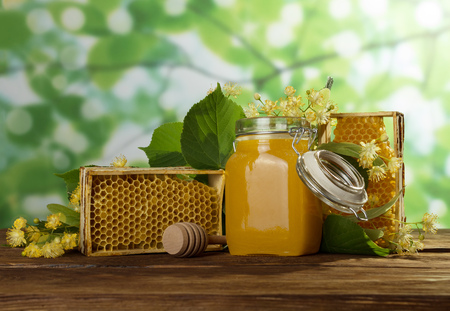 Honey in jar with lid, honeycomb on table, close-upの写真素材