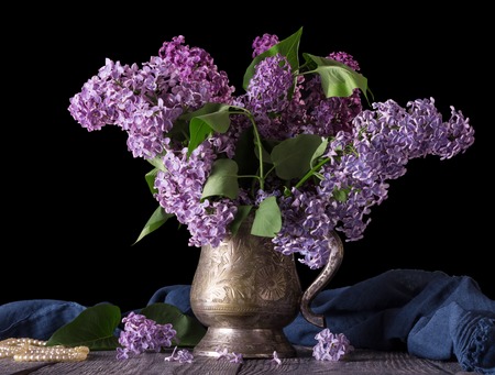 Lilac in an ancient vase, next to blue fabric and beads, isolated on blackの写真素材