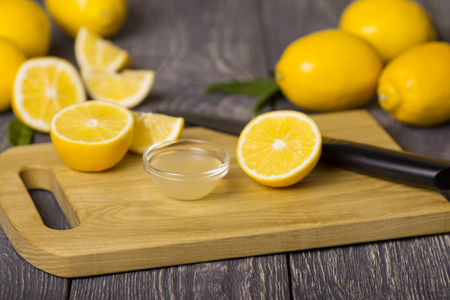 Pieces of lemon and knife on cutting Board, juice in bowlの写真素材