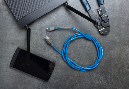 Router, smartphone, cable to connect and crimper on grey