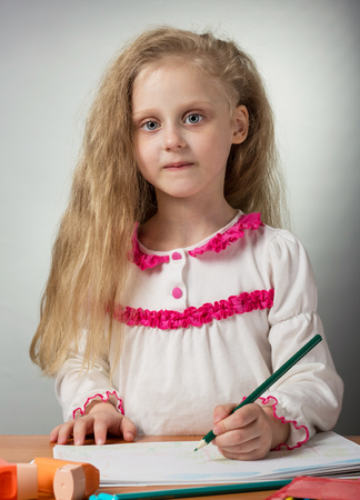 Adorable little blonde girl draws sitting at tableの写真素材