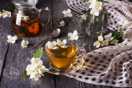 Herbal tea in teapot and Cup, Jasmine flowers scattered on wooden tableの写真素材