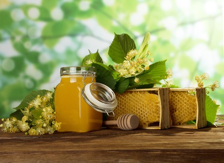 May honey in jar, wax honeycomb in frame and fragrant flowers on wooden tableの写真素材