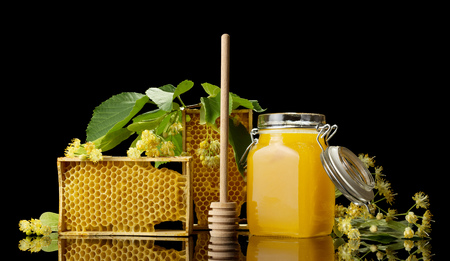 Bee honey in jar with lid, honeycomb and wooden stirrer isolated on blackの写真素材