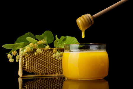 Fresh spring-harvested honey in the jar,next to wooden spoon and frame isolated on blackの写真素材