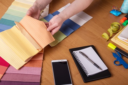 Hands dressmakers pick up fabric for sewing, near of tools and notebookの写真素材