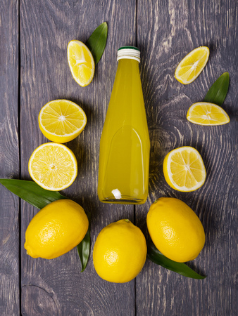 Bottle of lemon juice, whole lemons and pieces around it, against gray surfaceの写真素材