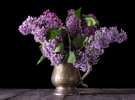 Bouquet of lilac in an old vase isolated on black backgroundの写真素材