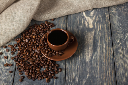 Cup of coffee, scattered grains on wooden surface, next to burlapの写真素材