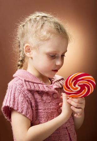 Little curly blonde girl holding sweet candyの写真素材