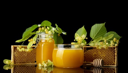 Two glass jars with honey and blossom of linden isolated on blackの写真素材