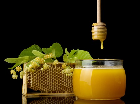 Drop of amber honey flows from wooden stirrer into jar, isolated on blackの写真素材
