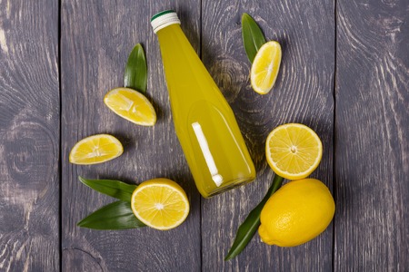 Yellow juicy lemons and bottle of lemon juice on grey backgroundの写真素材