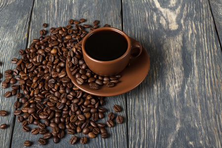 Coffee in ceramic Cup, coffee beans scattered near, on wooden tableの写真素材