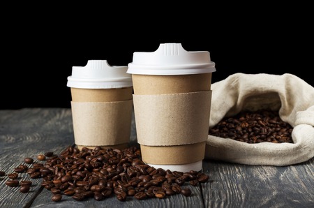 Two single-use container for hot drinks to take away, on background of coffee beansの写真素材