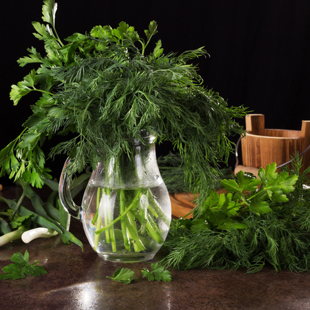 Bundle of fresh parsley and dill stands in jug with water, isolated on blackの写真素材