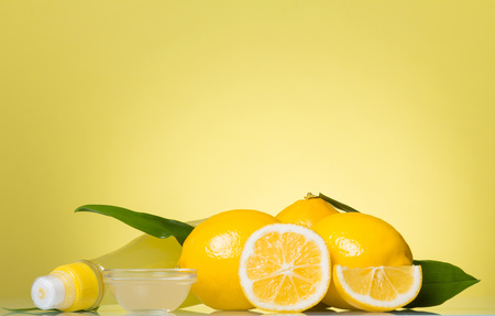 Lemon juice in bottle and small bowl, citrus fruit on yellow backgroundの写真素材