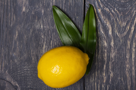 Bright yellow lemon with leaves on grey wooden surfaceの写真素材