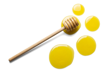Large and small drops of fresh honey, wooden stirrer isolated on whiteの写真素材