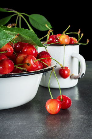 Bowl and mug are filled with ripe, washed cherries with petioles, on grey surfaceの写真素材