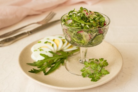 Salad of arugula and radish with sesame and egg in glass salad bowl, on tableclothの写真素材