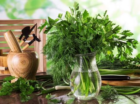 Bouquet of fresh, wet greens in jug, next to wooden stupa and onions on surfaceの写真素材