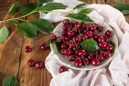 Large ripe cherries with tails in ceramic dish, on table with clothの写真素材