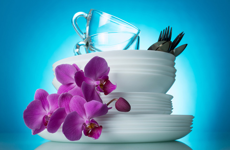 Sparkling clean white dishes and a branch of an orchid on a blue backgroundの写真素材
