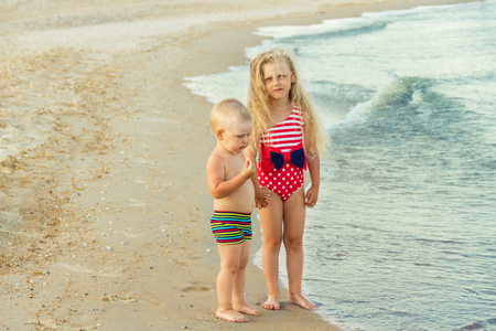 Brother and sister on a sandy light beach walk on the waterの写真素材