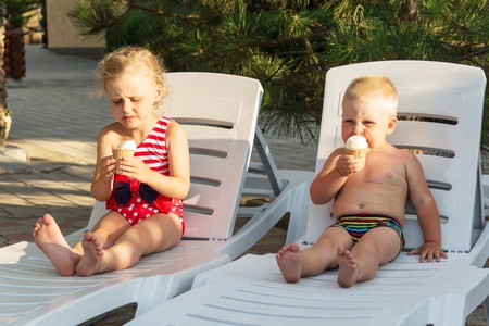 Happy children on a hot day eat ice cream on a white chaiseの写真素材