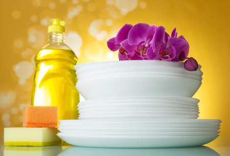 Means for washing dishes and a stack of clean plates on a beautiful yellow backgroundの写真素材