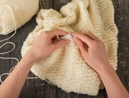 Hands knit a large warm woolen plaid of white yarn on the table. Hobby. Handmadeの写真素材