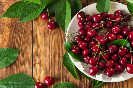 Juicy berries of sweet cherry with leaves on a wooden table. Top view with copy spaceの写真素材