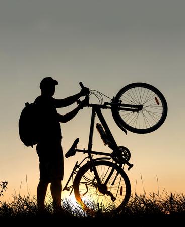 Silhouette of a cyclist man with a backpack at sunset with a bicycleの写真素材
