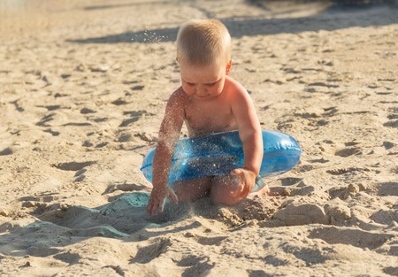 Blonde boy playing with sand on a sunny hot beachの写真素材