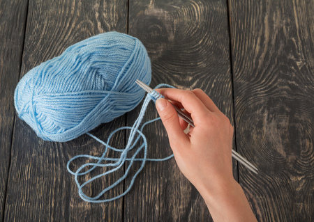 A female hand holds a crochet hook for blue wool thread on dark boards